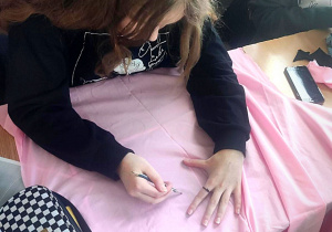 Uczennica odrysowuje na tkaninie kształt laleczki od szablonu.